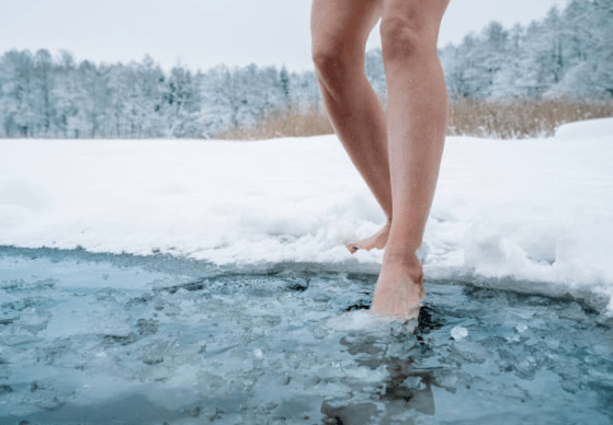 bare feet stepping into icy water from a snowy bank